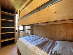 A bunk bed room with wooden walls, a window, and a shelf unit.