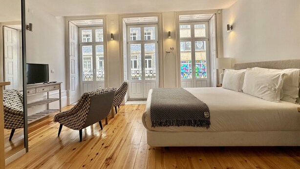 A bedroom with a bed, a desk with a TV, two chairs, and large windows with decorative glass doors.