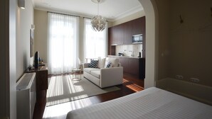 A modern hotel room with a large bed, a sitting area with a sofa and a coffee table, a kitchenette, and a large window with sheer curtains. - Superior Studio with Balcony in Bolhão Market (Oporto)