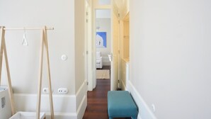A hallway with a wooden bench, a clothes rack, and a white wall with a light switch. - Exceptional Two-Bedroom, Apart in Bolhão Market (Oporto)