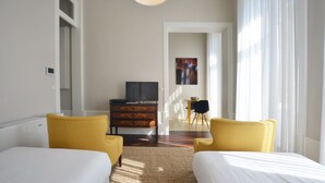 A hotel room with two beds, a dresser, a television, and a view of the outside through a door. - Twin Studio with Balcony in Bolhão Market (Oporto)