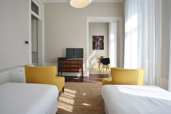 A hotel room with two beds, a dresser, a television, and a dining area with chairs.