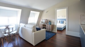 A modern living room with a sofa, a dining table with chairs, a TV stand, and a bed with a blue headboard. - Two-Bedroom Family Ap in Bolhão Market (Oporto)