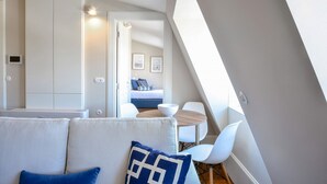 A modern, well-lit room with a sofa, a dining table, and a view of a bedroom with a bed and a wall-mounted light fixture. - Two-Bedroom Family Ap in Bolhão Market (Oporto)