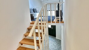 En trætrap med hvide gelændere fører op til et soveværelse med seng og skrivebord.