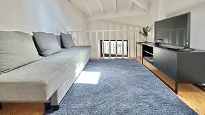 En moderne stue med en grå sofa, et fladskærms-tv på et træstel og et blåt tæppe.
