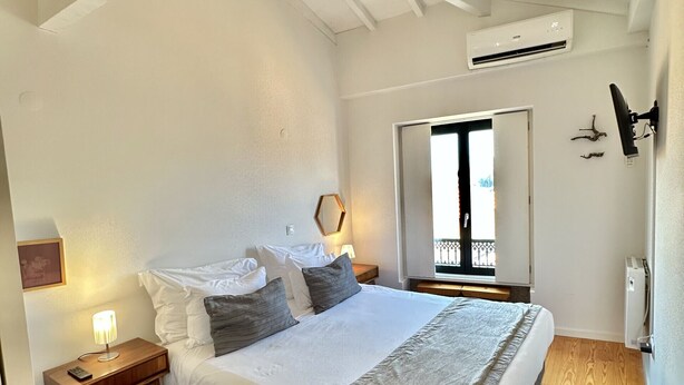 Una camera da letto con un letto, pavimento in legno, pareti bianche e un condizionatore d'aria.