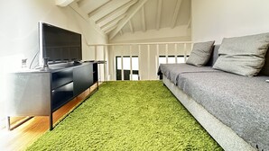 Un soggiorno moderno con una TV a schermo piatto, un divano grigio e un tappeto verde.