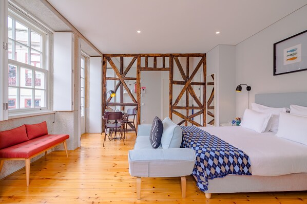A modern bedroom with a large bed, a red sofa, and a wooden partition wall. - Superb Studio with Balcony at the heart of Porto (Oporto)