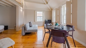 A spacious living area with a wooden floor, a grey sofa, a dining table with chairs, and a TV. - Amazing Duplex Two-Bedroom Apart with Views (Oporto)