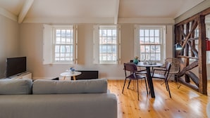 A modern living room with a sofa, a dining table with chairs, and large windows with open shutters. - Amazing Duplex Two-Bedroom Apart with Views (Oporto)