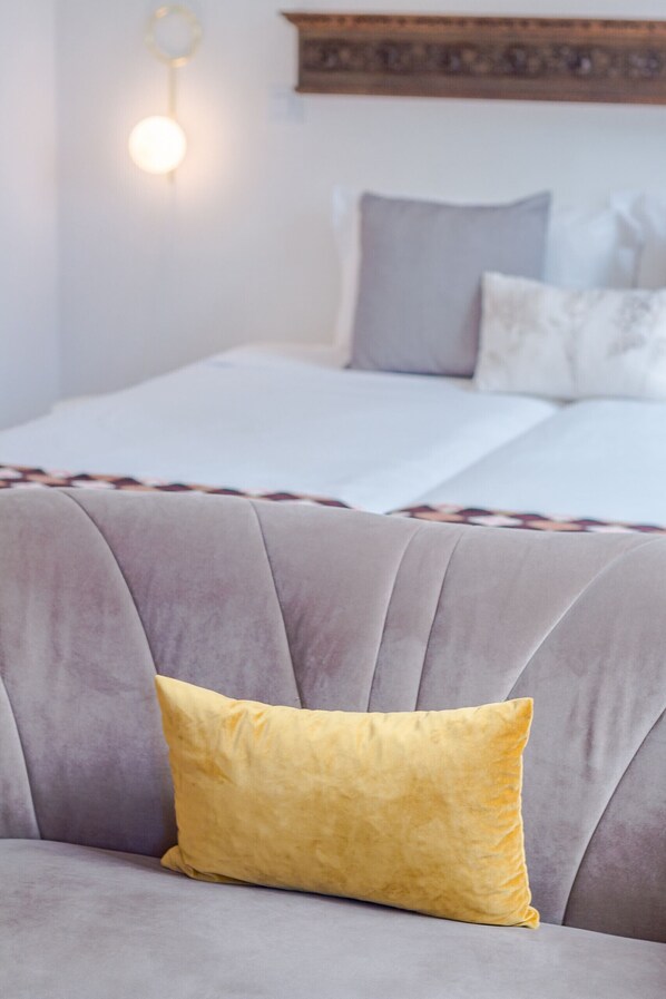 Una habitación con un sofá gris, un cojín amarillo y una cama con ropa de cama blanca.