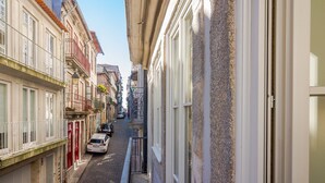 A narrow street with buildings on both sides, a white car parked on the left, and a narrow alleyway between the buildings.
