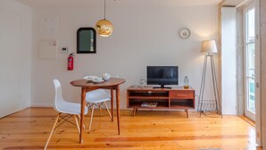 Un salon moderne avec une table à manger en bois, des chaises blanches, un téléviseur et un lampadaire.