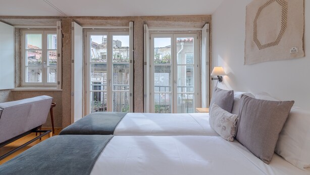 Une chambre avec un grand lit, une table de chevet, une lampe et une vue sur l’extérieur grâce à des fenêtres ouvertes.