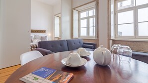A dining area with a wooden table, two white teapots, and a magazine. There is a sofa and a window with a view. - Comfy Twin Studio in Clérigos Tower (Oporto)