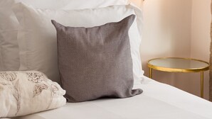 A neatly made bed with white and patterned pillows, a small round table, and a wall-mounted light fixture. - Comfy Twin Studio in Clérigos Tower (Oporto)
