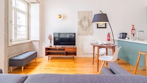 A modern living room with a television, sofa, bench, and dining area with chairs and a table. - Comfy Twin Studio in Clérigos Tower (Oporto)