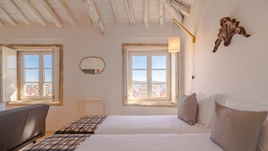 Une chambre avec deux lits, une vue sur la ville grâce à de grandes fenêtres et un plafond en bois.