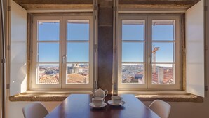 Un coin repas avec une table et des chaises, deux fenêtres donnant sur la ville et une théière posée sur la table.