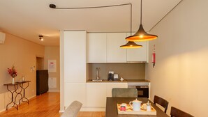 Une cuisine moderne avec des meubles blancs, une table à manger avec des chaises et des luminaires suspendus.