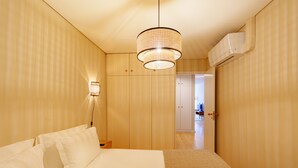 Une chambre d’hôtel avec un lit, un luminaire suspendu, un climatiseur fixé au mur et une porte donnant sur une autre pièce.