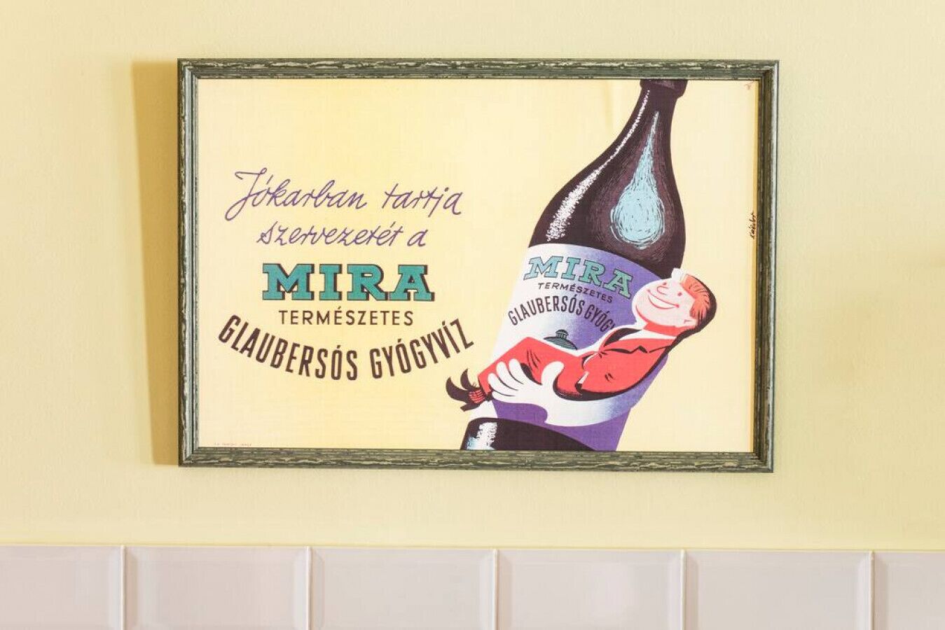 Ein gerahmtes Kunstwerk zeigt eine Flasche MIRA Bier, die von einer Person gehalten wird.