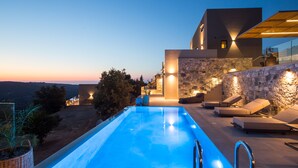 Un'area piscina moderna con parete in pietra, sedie a sdraio e vista sul paesaggio.