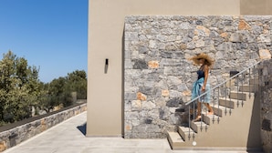 Una donna scende una scala in pietra all'interno di un edificio moderno, sullo sfondo un cielo sereno e alberi.