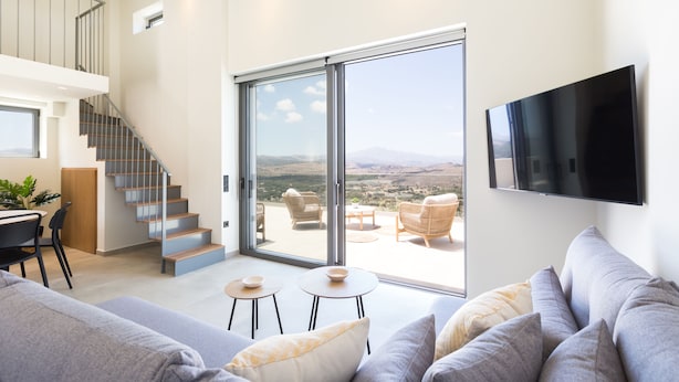 Un soggiorno moderno con divano, televisore a schermo piatto, una scala e un balcone con vista sul paesaggio.