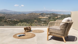Una sedia in vimini con un cuscino bianco su un balcone con vista su un paesaggio montuoso.