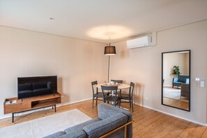 Una sala moderna con una televisión de pantalla plana, un sofá, una mesa de comedor con sillas, una lámpara colgante y un espejo grande.