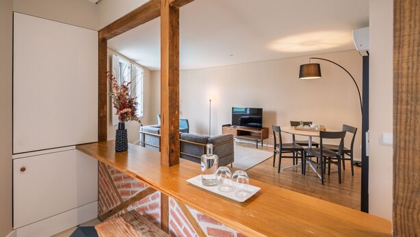 A modern kitchen with a wooden countertop, a dining area with a table and chairs, and a living room with a sofa and TV.