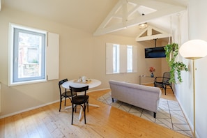 A dining area with a round table, chairs, a sofa, and a hanging plant.