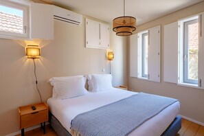 A bedroom with a bed, bedside tables, wall-mounted lights, and windows.