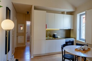 Een kleine keuken met witte kastjes, een spoelbak en een eethoek met een tafel en stoelen.