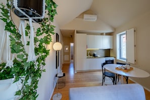 A compact kitchen with white cabinets, a dining area with a table and chairs, and a hallway leading to a bedroom.