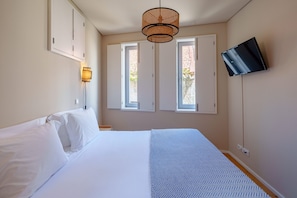 A bedroom with a bed, a wall-mounted TV, and two windows.