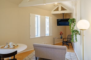 A dining area with a round table, chairs, a sofa, and a TV mounted on the wall.