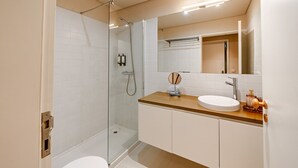 A modern bathroom with a glass-enclosed shower, a white sink, and a wooden vanity. - Comfortable 1BR Apt for 3 with balcony in Center (Oporto)