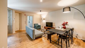 A modern living room with a sofa, dining table, chairs, a TV, and a lamp. - Comfortable 1BR Apt for 3 with balcony in Center (Oporto)