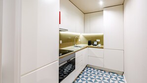 A compact kitchen with white cabinets, a black and white patterned floor, and a small countertop. - Comfortable 1BR Apt for 3 with balcony in Center (Oporto)