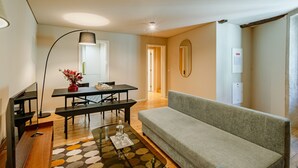 A modern living room with a sofa, a dining table, and a TV. - Comfortable 1BR Apt for 3 with balcony in Center (Oporto)