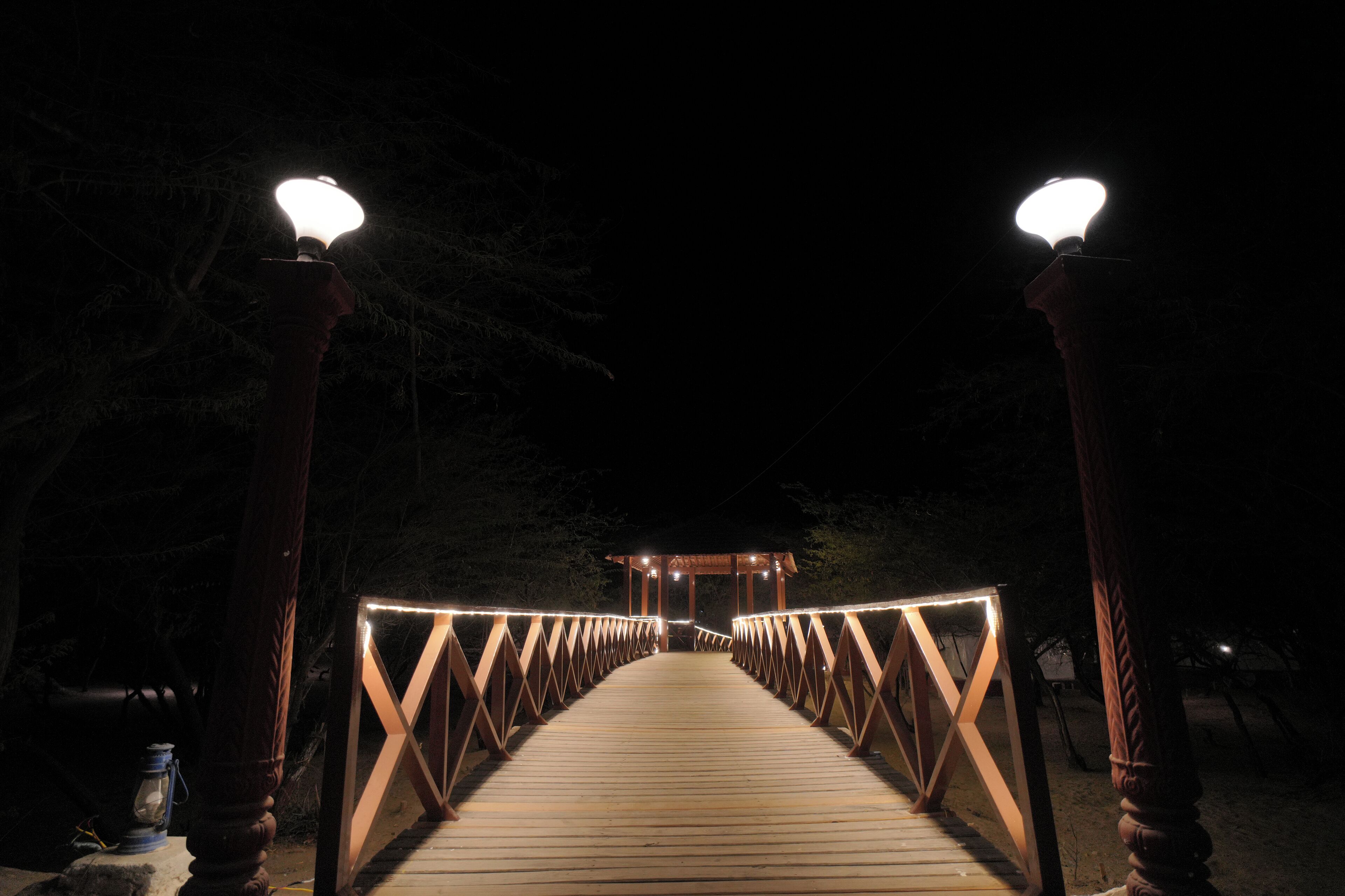 Un puente de madera con barandillas e iluminación que conduce a una zona cubierta.