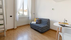 A room with a patterned sofa, a dining table with chairs, a window with curtains, and a thermostat on the wall. - GuestHost - Cozy APT on 2 levels Milan-Corso Magenta! (Milano)