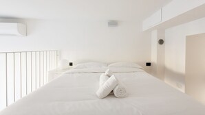 A hotel room with a bed, pillows, a rolled towel, a nightstand, and a wall-mounted air conditioning unit. - GuestHost - Cozy APT on 2 levels Milan-Corso Magenta! (Milano)