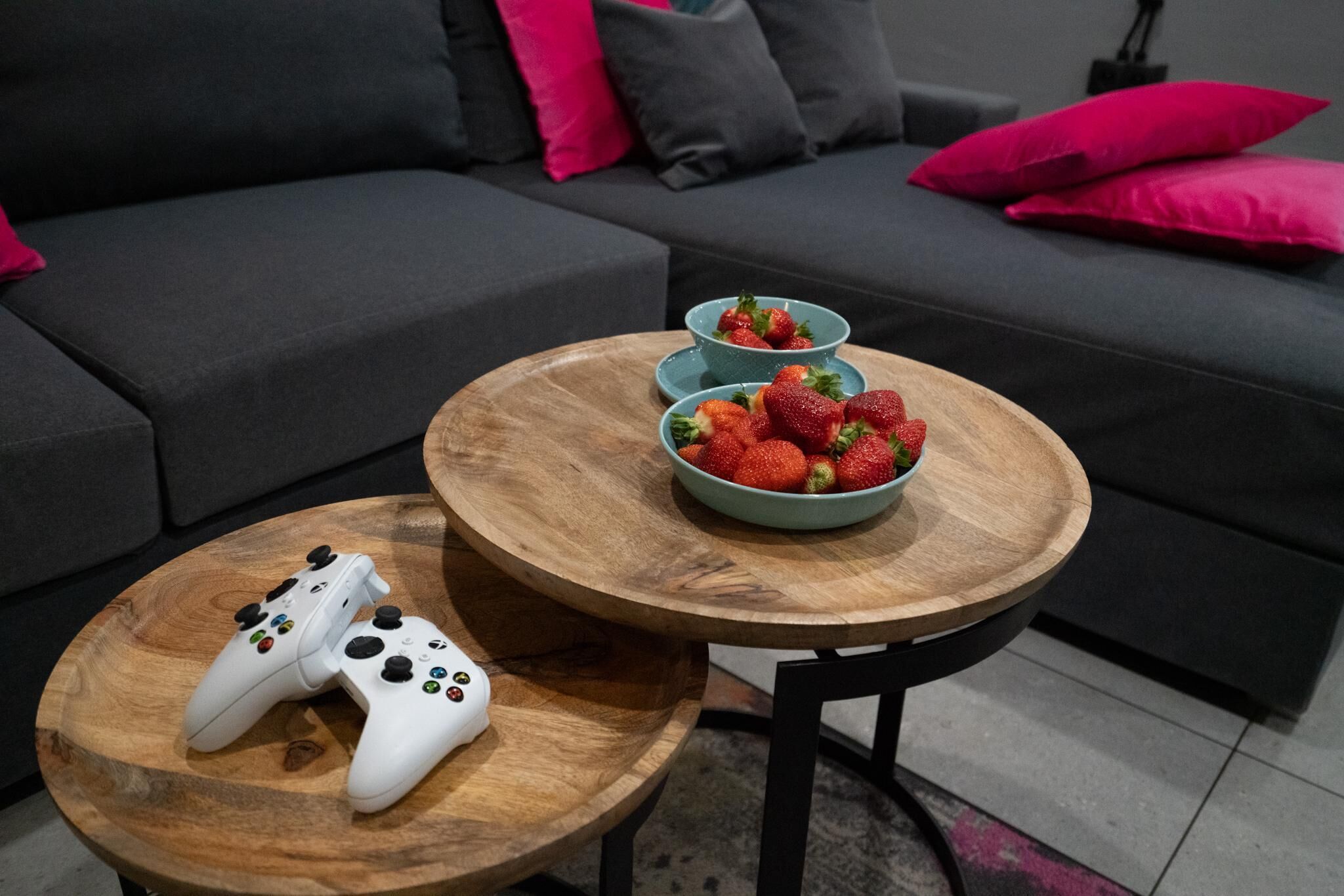Un salon moderne avec un canapé gris, deux tables basses en bois et un saladier rempli de fraises posé sur l’une des tables.