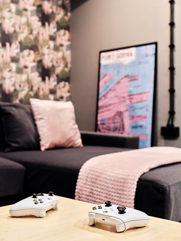 A bedroom with a bed, pillows, a blanket, and two white gaming controllers on a table. - Hola Gdynia (Gdynia)