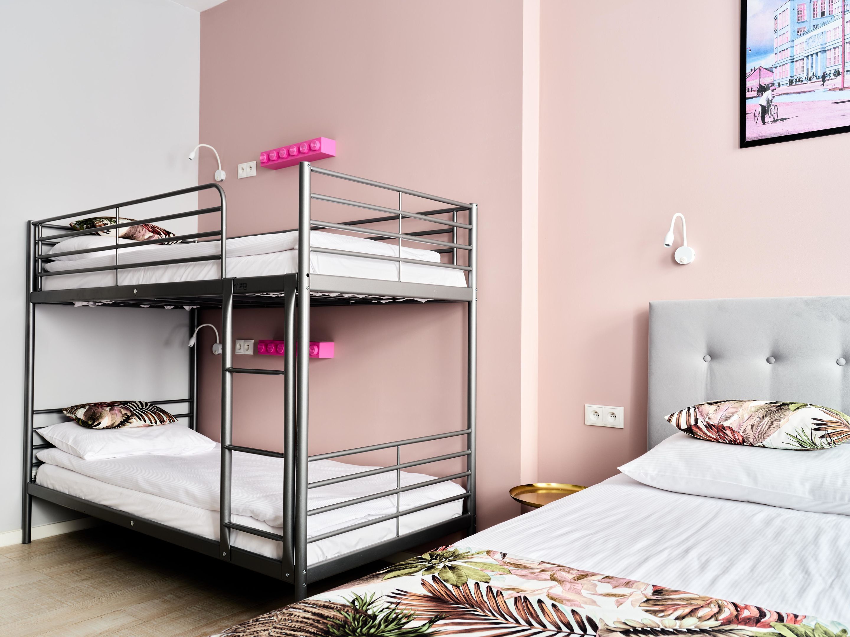 A bunk bed with a pink wall and a single bed with a floral pillow.