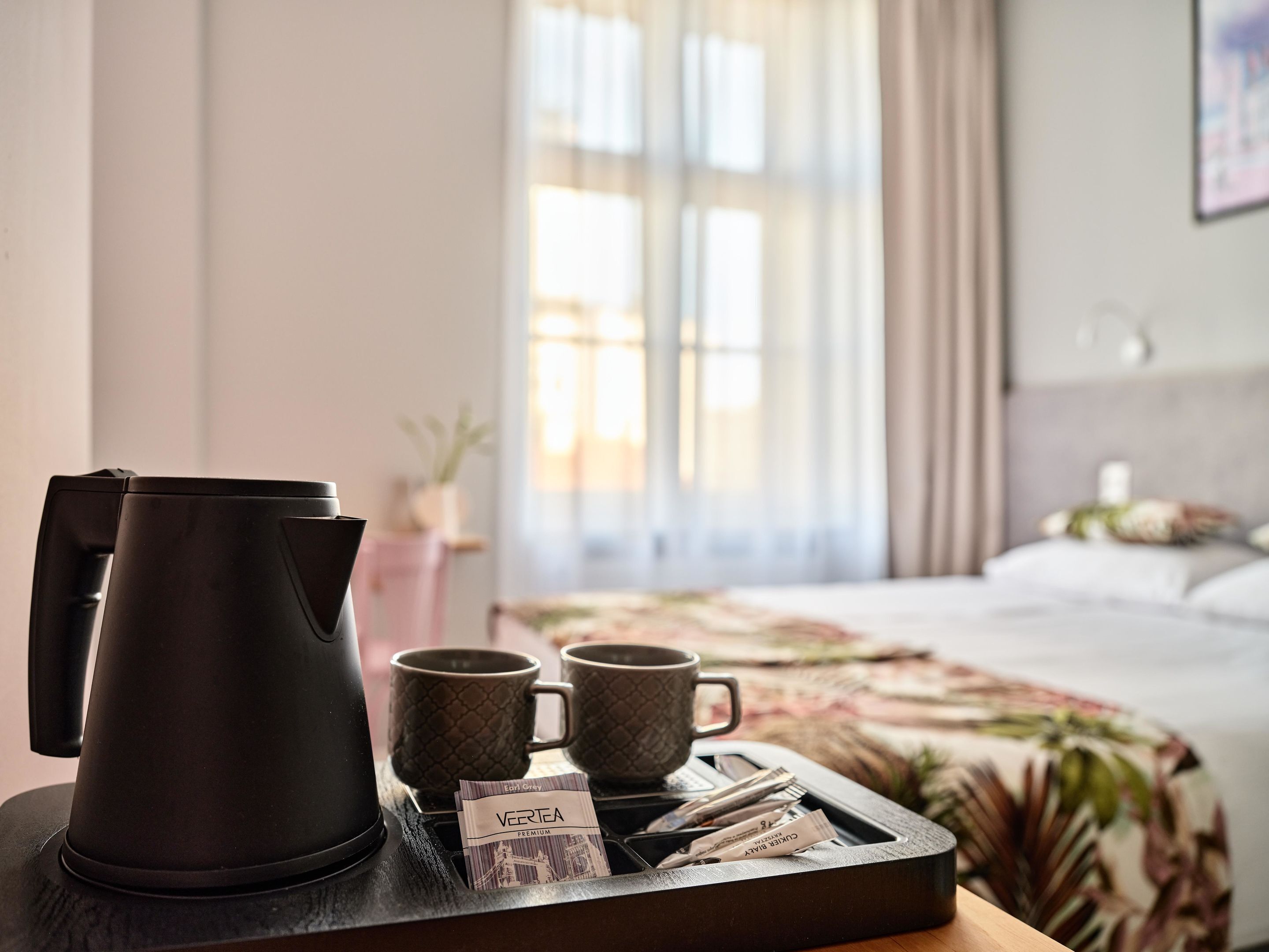 A hotel room with a bed, a coffee maker, two mugs, and tea packets on a tray.